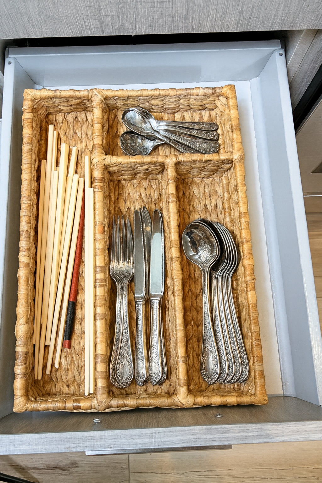 wicker water hyacinth cutlery tray with silverware and chopsticks inside a drawer.