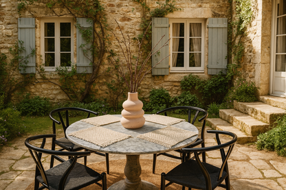 Boho macrame woven placemats on Round stone table with chairs in front of a stone building