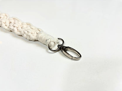 A close-up of a handwoven macramé camera strap in beige, featuring a clasp.